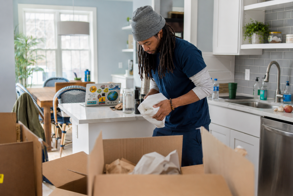 Professional Rochester Hills movers carefully packing household items in a modern kitchen during a residential move with moving boxes, packing paper, and natural daylight.